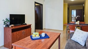 A living room with a TV, wooden furniture, a dining area with chairs and a table, and a kitchen in the background. - Naut 310 - Nautilius (Swinoujscie)