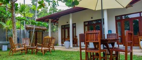 Un patio al aire libre con mobiliario de madera, un gran paraguas y un edificio blanco con columnas y ventanas.