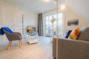 A modern living room with a sofa, armchair, TV, and a small table. - Apartment 7 Moby Dick (ID 433) (Sankt Peter-Ording)