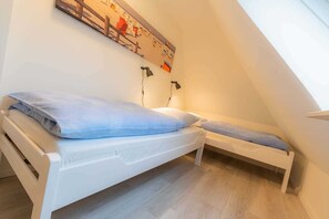 A small, white, loft-style bedroom with two single beds, a wooden floor, and a sloped ceiling. - Apartment 7 Moby Dick (ID 433) (Sankt Peter-Ording)