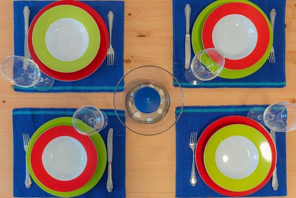 A dining table set with four plates, each with a red and green rim, and a clear glass centerpiece.