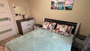 A bedroom with a bed, a dresser, a nightstand, and a mirror. There are three wall-mounted pictures above the bed. - Lovely Brand New Apartment with 2 Rooms and Balcony  (Chișinău)