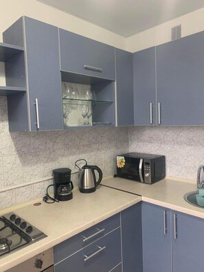 Una cocina con armarios azules, microondas, cafetera y estufa a gas.