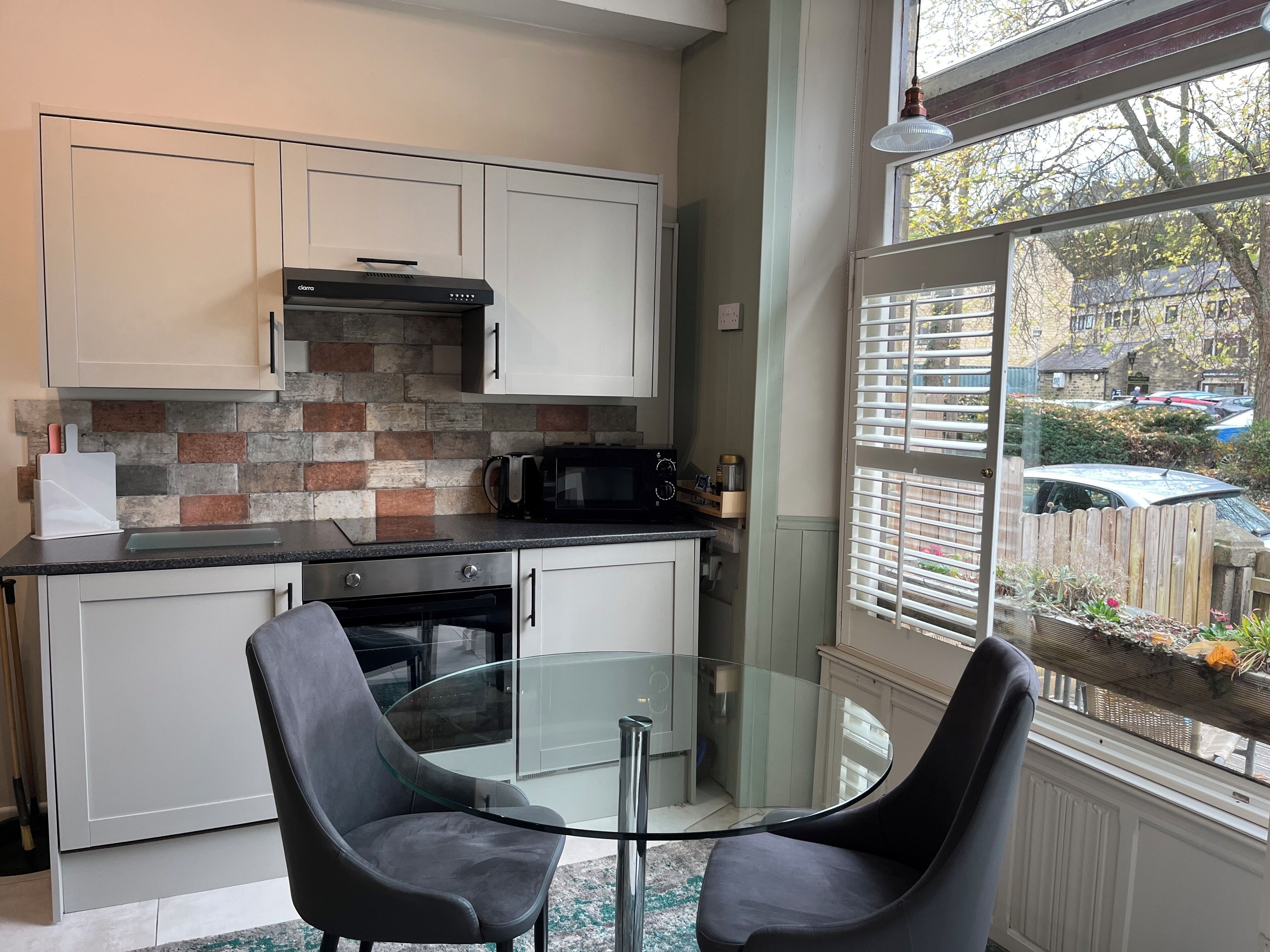 A compact kitchen with white cabinets, a brick backsplash, and a glass table with two chairs.