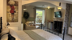 Un dormitorio con cama, lámpara de escritorio, sillón de cuero, televisión, chimenea y un cuadro en la pared.