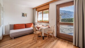 A room with a sofa, two chairs, a table, a window with curtains, and a view of mountains. - Holiday Apartment 'Camping Passeier Apfelblüte' with Mountain View, Garden & Wi-Fi (Saltaus)