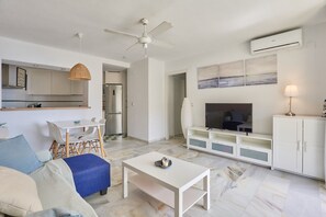 A modern living room with a white sofa, a coffee table, a TV, and a ceiling fan.