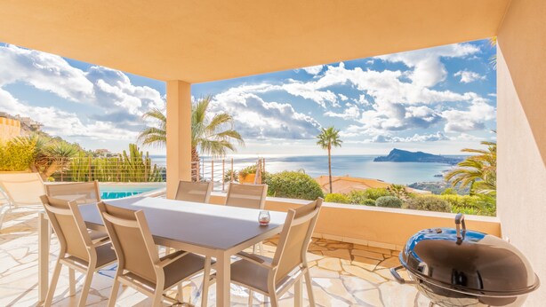 Eine Terrasse im Freien mit Tisch, Stühlen, einem Grill und Blick aufs Meer.