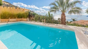 Ein Pool mit Blick auf das Meer und eine gebirgige Landschaft im Hintergrund.