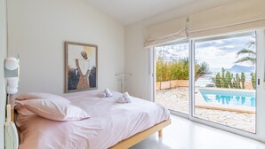 Ein Schlafzimmer mit Bett, einem Gemälde und Blick auf einen Swimmingpool.