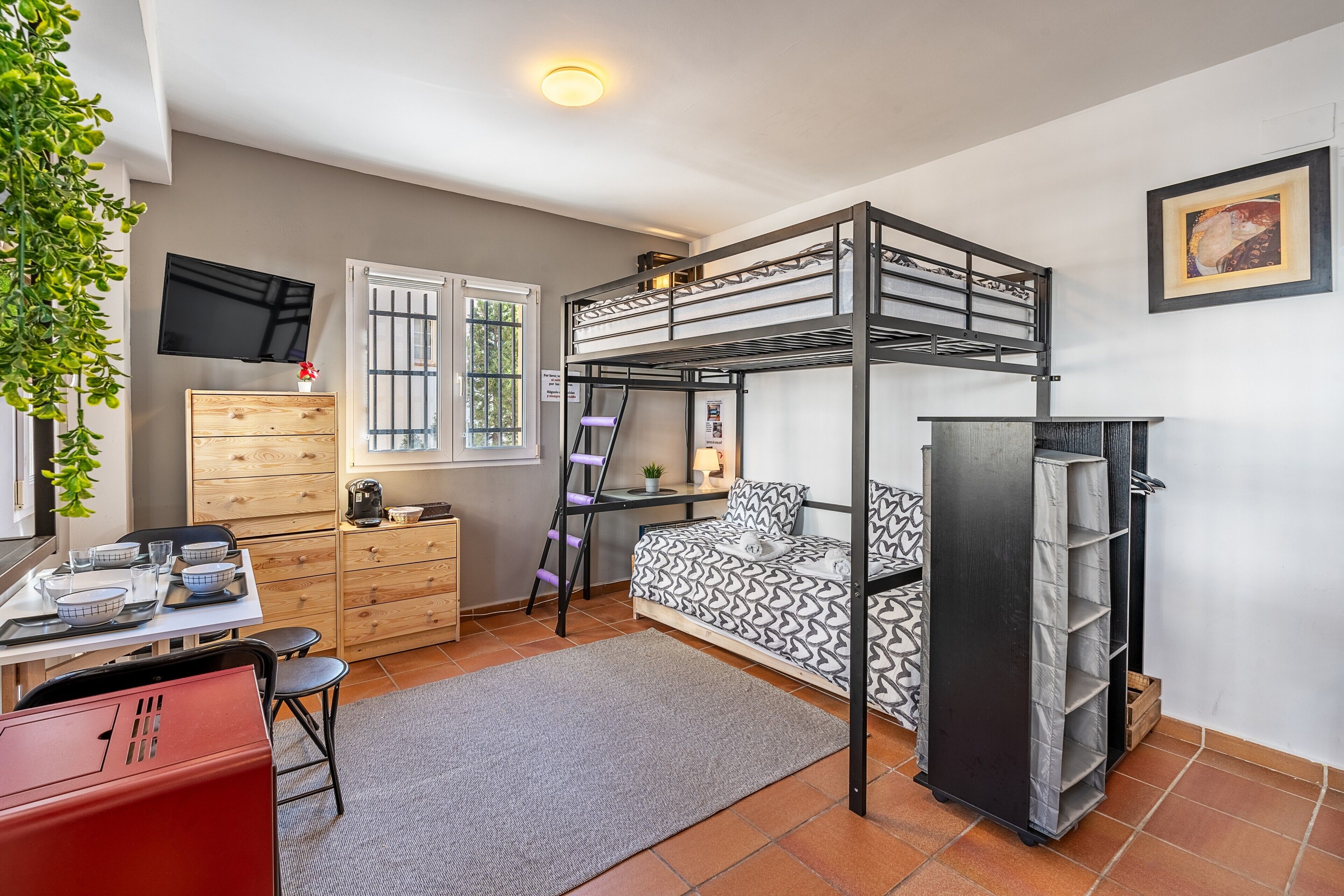 A bunk bed room with a desk, chair, and a TV on the wall.