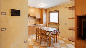A compact kitchen with wooden cabinets, a tiled floor, a dining table with chairs, and a built-in TV shelf. - Apartment "Piz Filone" with Mountain View, Wi-Fi (Livigno)
