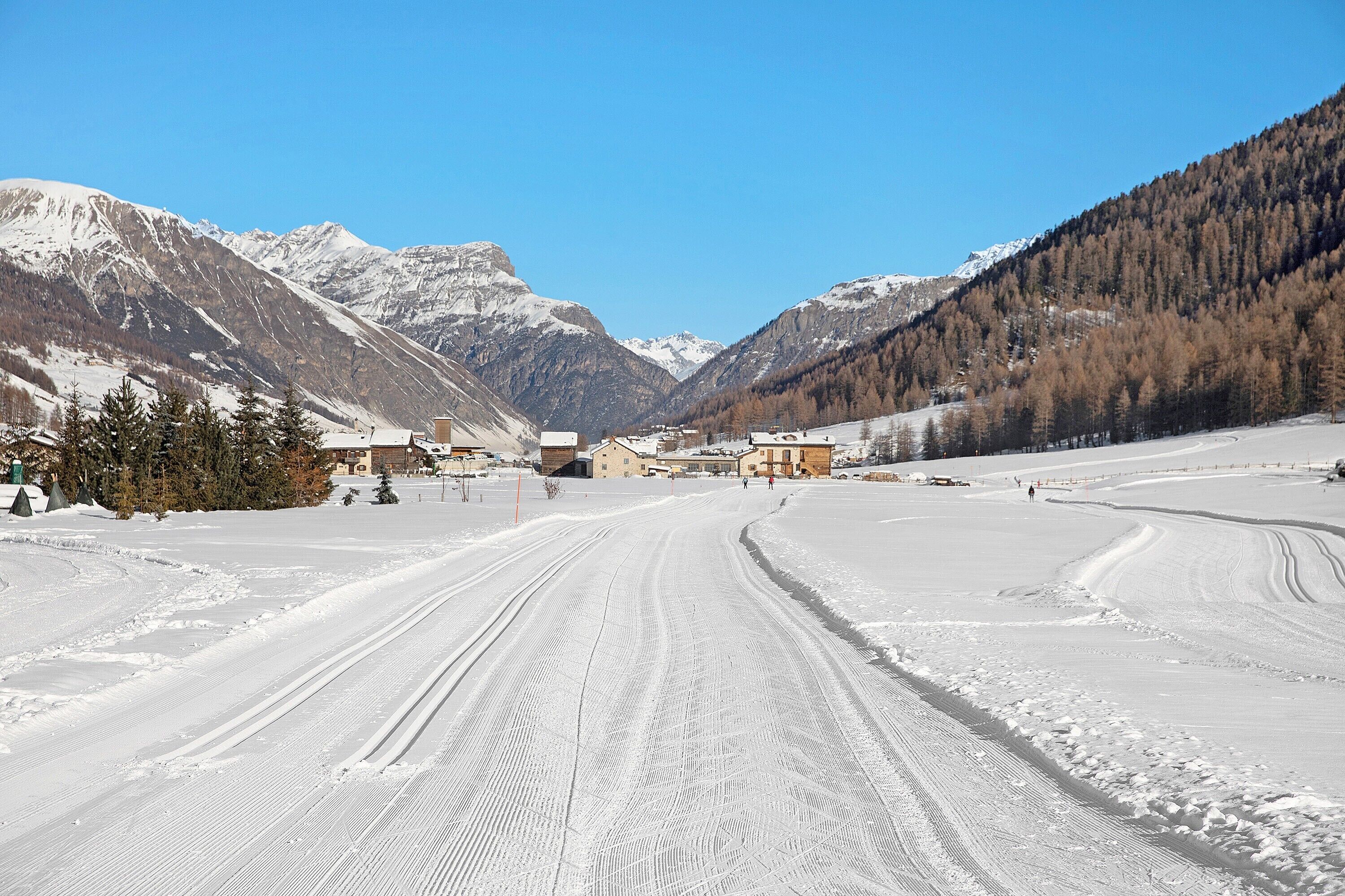 A snow-covered road leading to a building with a clear view of mountains.