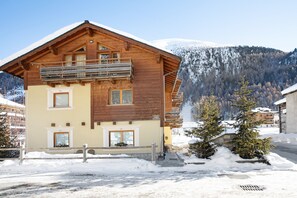 Un chalet en bois doté d’un balcon, d’une entrée en pierre et offrant une vue sur des montagnes enneigées.