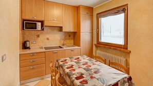 A compact kitchen with wooden cabinets, a microwave, a sink, and a table with a quilt. - Apartment "Piz Filone" with Mountain View, Wi-Fi (Livigno)