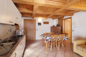 A kitchen with wooden ceiling beams, a dining table with chairs, a sofa, and a tiled floor.