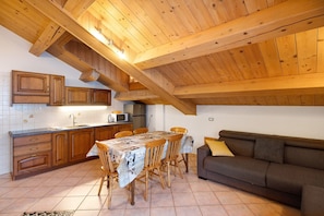 A kitchen with wooden cabinets, a dining table with chairs, a sofa, and a microwave.