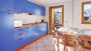A modern kitchen with blue cabinets and a dining area with a table and chairs. - Paradisin Apartment with Mountain Views (Livigno)