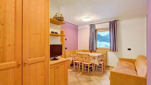 Un meuble en bois abritant un téléviseur, une table à manger avec des chaises, un canapé et une fenêtre donnant sur les montagnes.