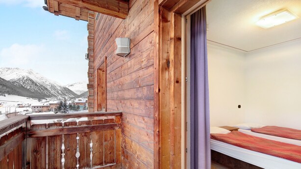 Une cabane en bois avec un balcon, un lit avec une literie rouge et une vue sur la montagne.
