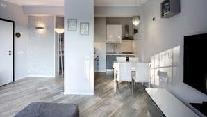 A modern kitchen with white cabinets, a dining area with white chairs, and a large flat-screen TV.