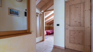 A hallway with a wooden door, a framed picture on the wall, and a bedroom visible through an open door. - Apartment Stefano 2 with Mountain View, Wi-Fi & Garden (Livigno)
