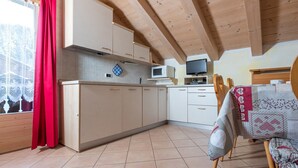 A kitchen with wooden cabinets, a microwave, a television, and a dining area with a table and chairs. - Apartment Stefano 2 with Mountain View, Wi-Fi & Garden (Livigno)