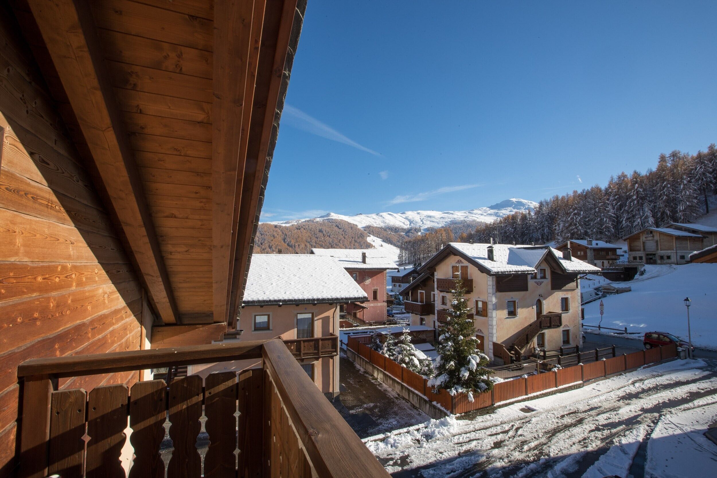 A wooden balcony overlooking a snow-covered village with houses and mountains in the background.
