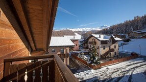 A wooden balcony overlooking a snow-covered village with houses and mountains in the background. - Apartment Stefano 2 with Mountain View, Wi-Fi & Garden (Livigno)