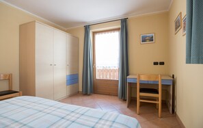 Une chambre à coucher comprenant un lit, un bureau, une armoire et une fenêtre avec des rideaux.