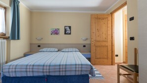 Un dormitorio con cama, una silla, una puerta de madera y dos lámparas fijadas a la pared.