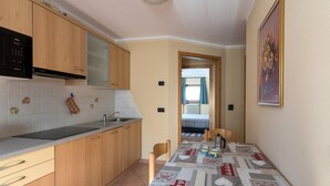 Una cocina con armarios de madera, un microondas negro, un lavabo y una mesa de comedor con mantel acolchado.