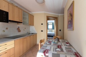 A kitchen with wooden cabinets, a black microwave, a sink, and a dining table with a quilted tablecloth.