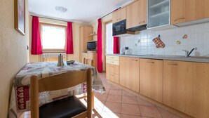 Una cocina con armarios de madera, microondas, una mesa con mantel y una ventana con cortinas rojas.
