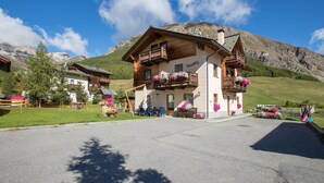 Un hotel de estilo chalé con balcones de madera, un telón de fondo de montañas y un camino de entrada pavimentado.