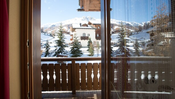 Una puerta de madera que da a un balcón con vistas a una montaña nevada y edificios.