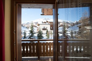 Une porte en bois donnant sur un balcon d’où l’on peut admirer une montagne enneigée et des bâtiments.