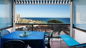 Uma varanda com mesa e cadeiras, vista para o mar e edifícios ao fundo.