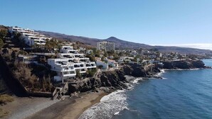 Uma vila costeira com edifícios brancos, uma praia e uma montanha ao fundo.
