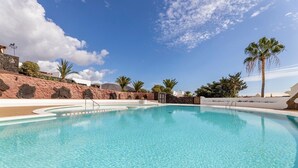 Ein klares, blaues Schwimmbecken mit einer Steinmauer und Palmen im Hintergrund.