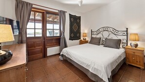 Ein Schlafzimmer mit Bett, Nachttischen, Deckenventilator, einem Fenster mit Vorhängen und einer Wanddekoration.
