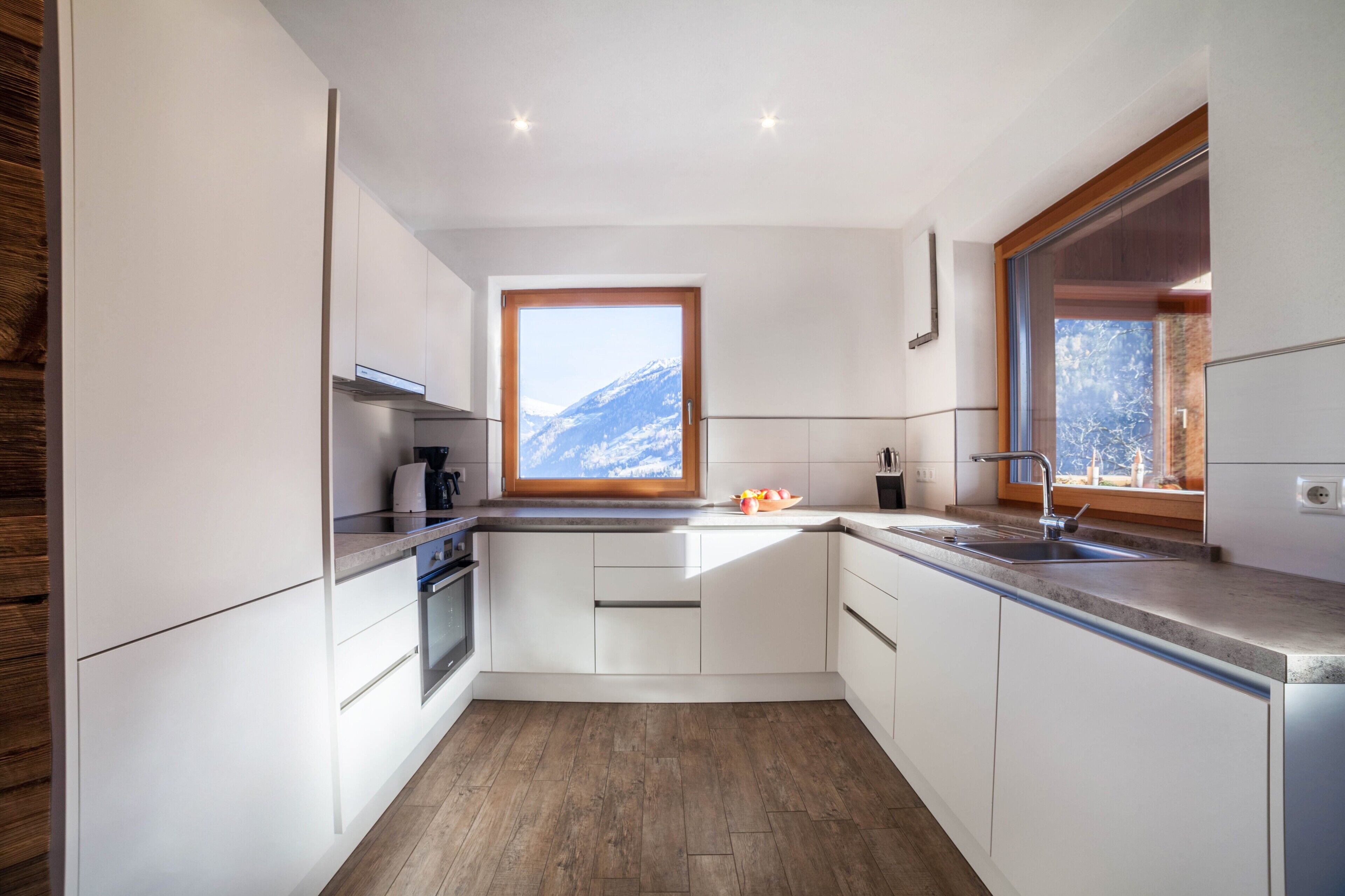 Une cuisine moderne avec des armoires blanches, un plancher en bois, une fenêtre donnant sur les montagnes et un four encastré.