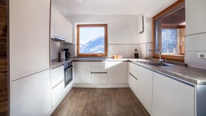 A modern kitchen with white cabinets, a wooden floor, a window with a mountain view, and a built-in oven.