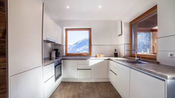 Une cuisine moderne avec des armoires blanches, un plancher en bois, une fenêtre donnant sur les montagnes et un four encastré.