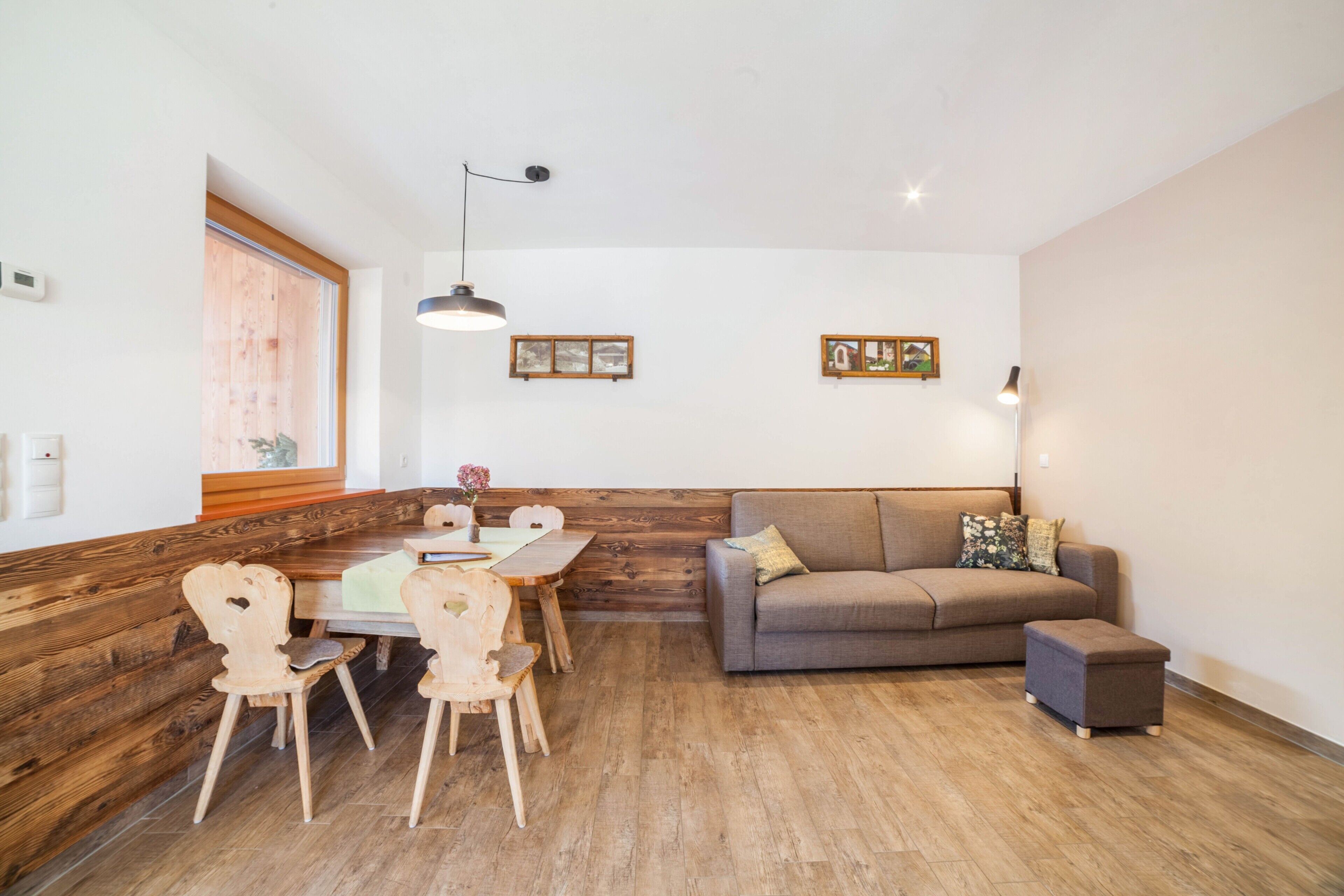 A modern interior with a wooden bench, a sofa, a dining table with chairs, and a small ottoman.