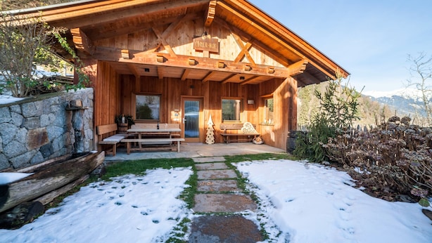 A wooden cabin with a stone foundation, a covered porch, and a stone pathway leading to the entrance.