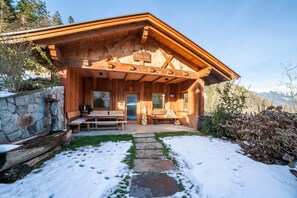 A wooden cabin with a stone foundation, a covered porch, and a stone pathway leading to the entrance.