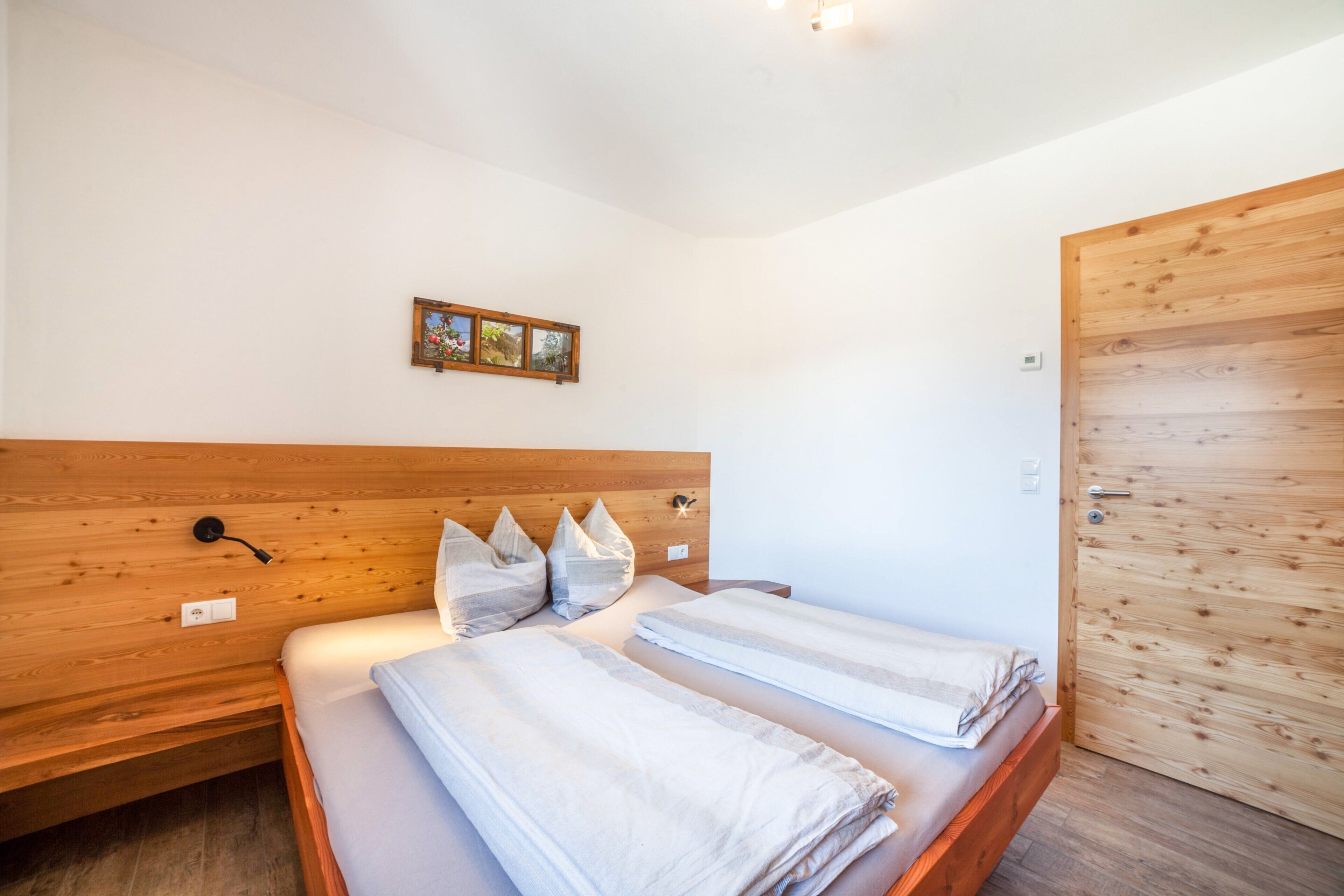 Une chambre avec deux lits, une tête de lit en bois, une porte en bois et un luminaire fixé au mur.