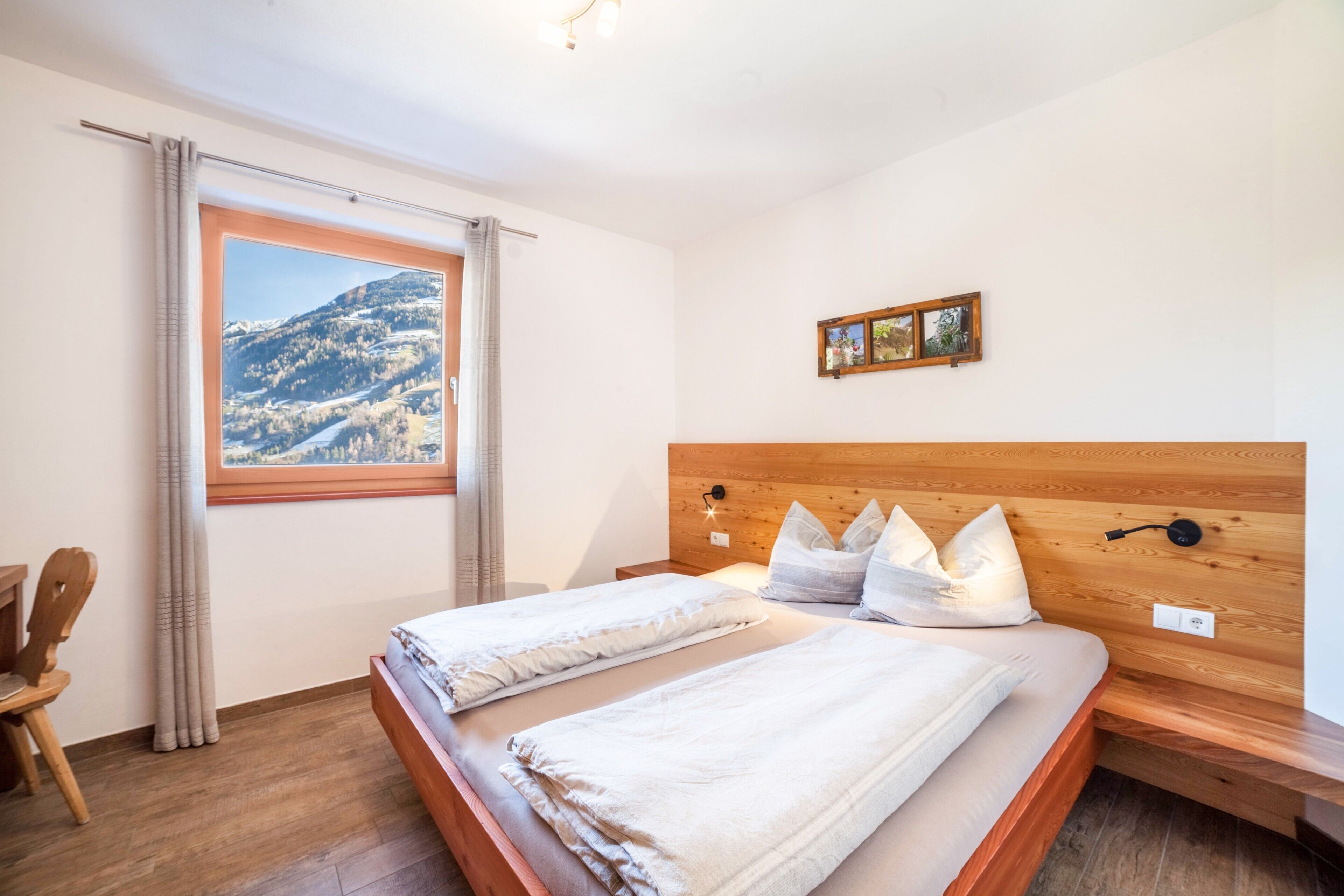 A bedroom with two beds, a wooden headboard, a window with a mountain view, and a small framed picture on the wall.