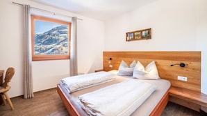 A bedroom with two beds, a wooden headboard, a window with a mountain view, and a small framed picture on the wall.